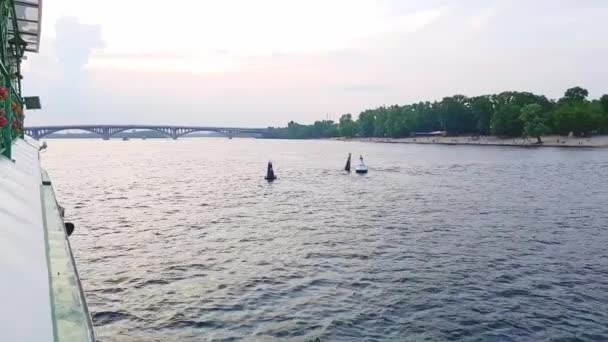 4К, корабль отплывает по широкой реке Днепра с большими мостами перед закатом — стоковое видео