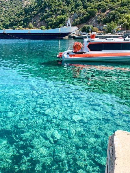 Un muelle al pie del Monte Athos en Grecia. Agua de mar clara, un buque de carga seca, un pequeño barco y un bosque en el fondo — Foto de Stock