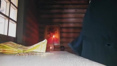 Ortodoks rahibi kutsal giysilerini giyer. Alacakaranlıktaki ahşap bir kilisenin mihrabının önünde dikilir.