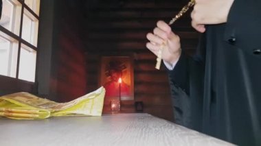 Ortodoks rahibi kutsal giysilerini giyer. Alacakaranlıktaki ahşap bir kilisenin mihrabının önünde dikilir.