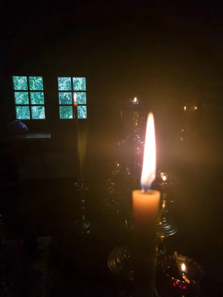 Et gult lys med en lang flamme i alteret i en ortodoks kirke nær tronen med en menorah overfor vinduet i skumringen. – stockfoto