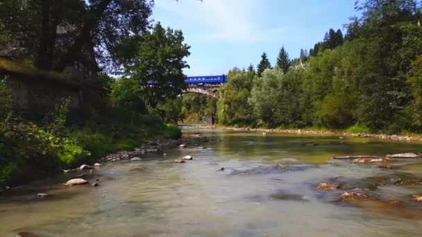 De trein passeert een stenen musta boven de berg, een ondiepe rivier met een snelle stroom in de Karpaten met een rotsachtige bodem op een zonnige dag. 4k schieten — Stockvideo