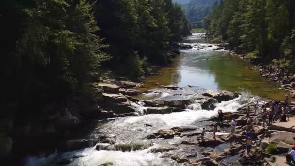 El flujo de agua entre las piedras. El agua clara cae rápidamente cuesta abajo fluyendo alrededor de piedras húmedas oscuras. Primer plano de la cascada vertiendo rocas negras. Hermosa cascada de montaña — Vídeo de stock