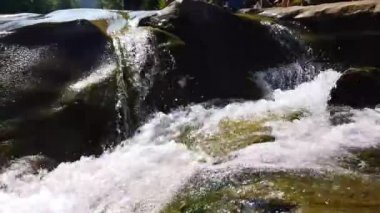 Taşlar arasında su akıntısı akar. Berrak su hızla karanlık ıslak taşlar etrafında akan yokuş aşağı düşmek. Siyah kayalarakan şelalenin yakın çekim. Güzel dağ şelalesi