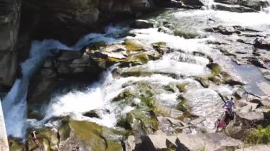 Taşlar arasında su akıntısı akar. Berrak su hızla karanlık ıslak taşlar etrafında akan yokuş aşağı düşmek. Siyah kayalarakan şelalenin yakın çekim. Güzel dağ şelalesi