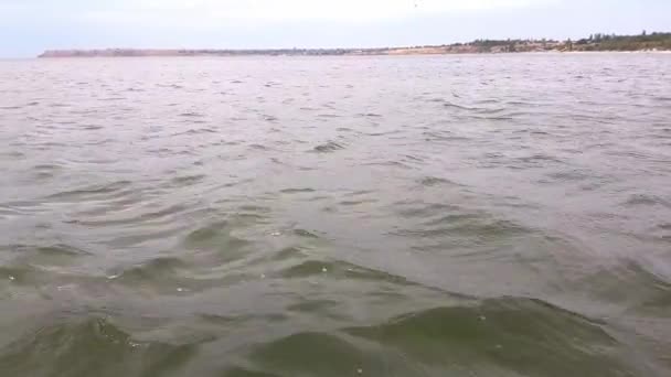 Um homem senta-se na cauda de um catamarã com as pernas ao mar na água em tempo calmo . — Vídeo de Stock