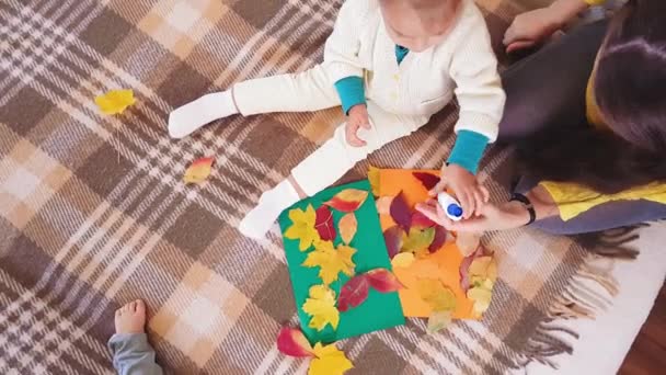 Young mother with children make autumn applique from autumn leaves. Little girl with mom glues autumn casting on a cardboard sheet. Making autumn applique at home. — Stock Video