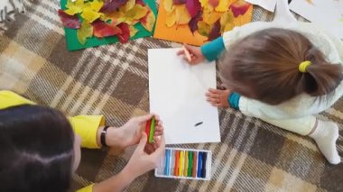 Genç anne ve kız yağ rengi pastel yazılar çiziyor. Beyaz kağıtlara sonbahar yazılıyor ve başvuru yapılıyor. Annesi olan küçük bir kız, beyaz kağıt üzerine sonbahar yazıtları çiziyor..