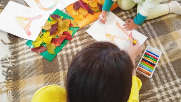 Mamma e figlioletta fanno applicazione autunnale dalle foglie autunnali. La bambina con mamma incolla la colata di autunno su un foglio di cartone. Fare applique autunno a casa . — Video Stock