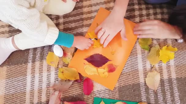 A mãe e a filha pequena fazem o aplique de outono de folhas de outono. Menina com mãe cola fundição de outono em uma folha de papelão. Fazendo aplique outono em casa . — Vídeo de Stock