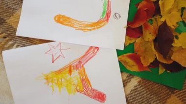 Genç anne ve kız yağ rengi pastel yazılar çiziyor. Beyaz kağıtlara sonbahar yazılıyor ve başvuru yapılıyor. Annesi olan küçük bir kız, beyaz kağıt üzerine sonbahar yazıtları çiziyor..
