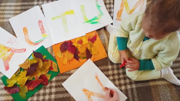 Genç anne ve kız yağ rengi pastel yazılar çiziyor. Beyaz kağıtlara sonbahar yazılıyor ve başvuru yapılıyor. Annesi olan küçük bir kız, beyaz kağıt üzerine sonbahar yazıtları çiziyor.. — Stok video