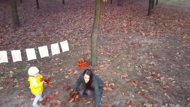 Mom with children toss up autumn leaves in the park near a garland of white paper leaves with the inscription Autumn painted with colorful paints. — Stockvideo