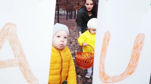 Mamma med barn samlar höstlöv i parken nära en krans av vita pappersblad med inskriptionen Hösten målad med färgglada färger. — Stockvideo