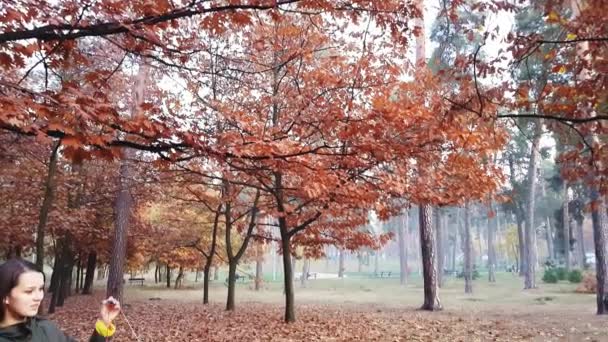 Mãe com uma pequena filha segurar uma grinalda de folhas brancas de papel com a inscrição Outono em cores coloridas de outono no parque da noite . — Vídeo de Stock