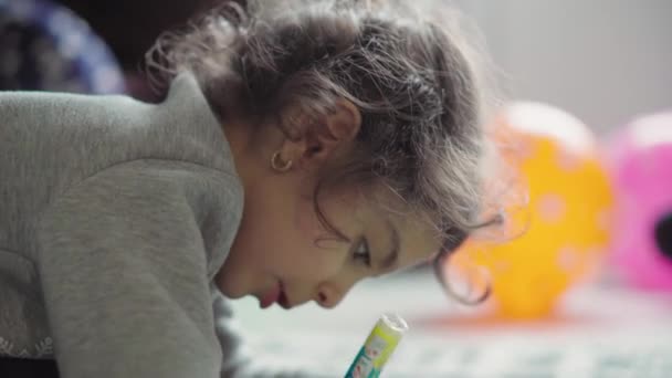 Infância, brincadeira, treinamento, conceito de auto-isolamento close-up dark-haired curly little six-year-old girl of Persian Middle Eastern appearance draw in notebook pencil lying on her stomach on floor . — Vídeo de Stock