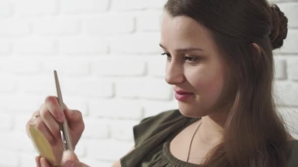 Moda y belleza, fiestas, cosmetología, concepto de estilo de vida - joven hermosa chica casual de tonos oscuros haciendo maquillaje marrones sus mejillas y sonrisas lindo sobre un fondo de ladrillo blanco. — Vídeos de Stock