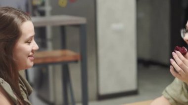 Kafeler ve restoranlar, evcillik, iletişim, akrabalar konsepti - iki genç kız kardeş akşam evde mutfak masasında oturmuş şekerlerle çay içerek sohbet ediyorlar. Konuşan kadınlar.