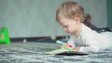 Çocukluk, oyun, eğitim, kendini izole etme konsepti. İki yaşında, sevimli, açık renk saçlı bir çocuk, karnının üzerine uzanmış bir kalem çizer. genel plan kopyalama alanı