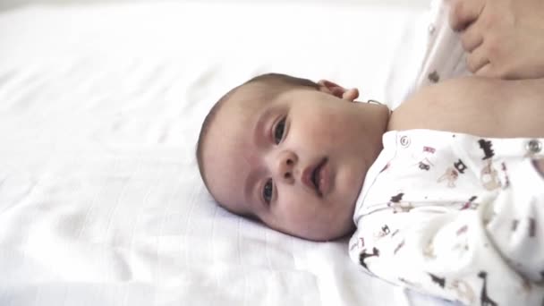 Infant, motherhood, development, childhood, training, pediatrics, medicine and health concept - close-up naked newborn lies wakes up mom puts baby in bodysuit. on white background. — Stock Video