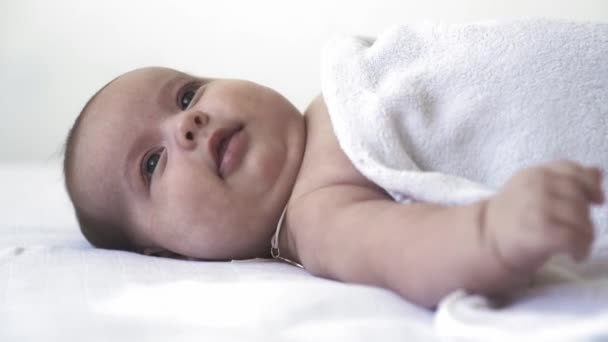 Baby, ontwikkeling, kindertijd, training, kindergeneeskunde, geneeskunde en gezondheid concept - close-up naakt pasgeboren baby ligt wakker op bed met verschillende grillen en emoties op witte achtergrond — Stockvideo