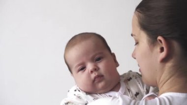 Bebek, annelik, gelişim, çocukluk, pediatri, tıp ve sağlık konsepti - kollarına beyaz elbise giymiş genç bir anne battaniyeye sarılmış ve çocuğu öpüyor.