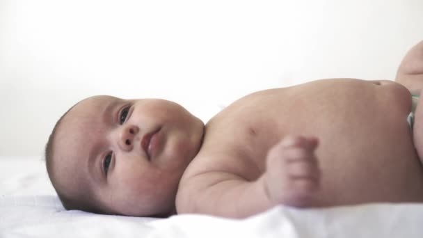 Spädbarn, utveckling, barndom, utbildning, pediatrik, medicin och hälsa koncept - närbild nakna nyfödda barn ligger vakna upp på sängen visar olika grimaser och känslor på vit bakgrund — Stockvideo