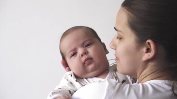 Bebek, annelik, gelişim, çocukluk, pediatri, tıp ve sağlık konsepti - kollarına beyaz elbise giymiş genç bir anne battaniyeye sarılmış ve çocuğu öpüyor. — Stok video