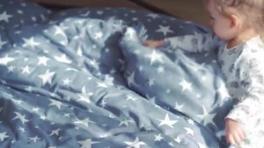 Çocukluk, yetiştirilme, bakım, temizlik konsepti. Üç yaşındaki küçük sarışın bir kız, bir sabah uykusundan sonra neşe dolu bir yatağı doldurur. Bebek odayı temizler..