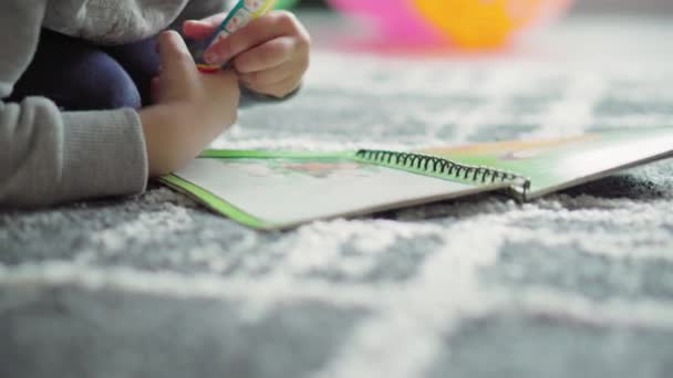 Infância, brincadeira, treinamento, conceito de auto-isolamento close-up dark-haired curly little six-year-old girl of Persian Middle Eastern appearance draw in notebook pencil lying on her stomach on floor . — Vídeo de Stock