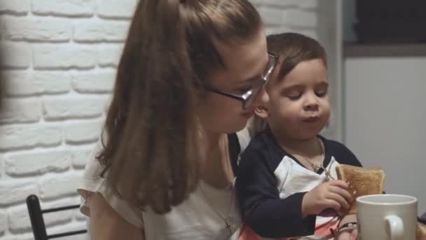 Moederschap, ouderschap, familie, voeding concept - Jonge leuke Perzische grote moeder van het Midden-Oosten verschijning met bril met kinderen is het eten in de keuken thuis. — Stockvideo