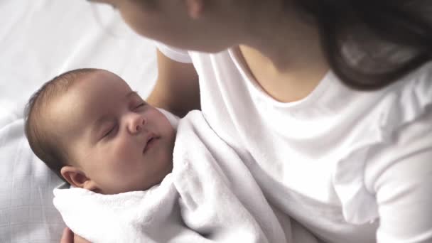 Bebé, maternidad, desarrollo, infancia, pediatría, medicina y concepto de salud - madre joven de cerca vestida de blanco sostiene en sus brazos al bebé recién nacido envuelto en caricias de manta y arrullos niño . — Vídeo de stock