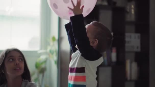 Crianças, celebração, aniversário, famílias grandes, jogos e conceito de entretenimento - crianças e adolescentes de diferentes idades e nacionalidades brincam com balões em quarto espaçoso contra a janela . — Vídeo de Stock