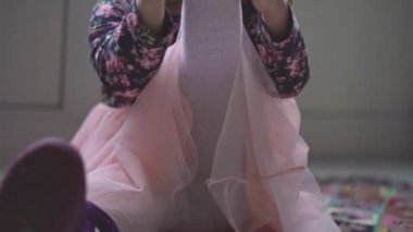 Çocukluk, oyunlar, gelişim, eğlence, giysi ve ayakkabı konsepti - pembe elbiseli ve beyaz taytlı küçük kız botlarını giyer, ayağa kalkar ve uzaklaşır.