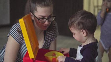 Annelik, çocukluk, beslenme, yemek, aile, bakım konsepti - orta plan koyu saçlı anne, iki yaşındaki Orta Doğulu çocuğunu yerde oturan yırtık kotlu kaşık tabakasından besliyor