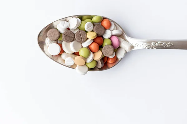 Medicine and health, treatment, pharmaceutics, coronavirus, pandemic, epidemic concept - layout one silver big tablespoon with multi-colored tablets and capsules on a white background copy space. — Stock Photo, Image