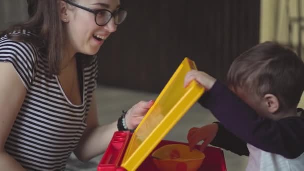 Maternité, enfance, alimentation, nourriture, famille, concept de soins - maman aux cheveux bruns du plan moyen nourrit son enfant de deux ans du Moyen-Orient à partir d'une assiette de cuillère en jean déchiré assis sur le sol — Video