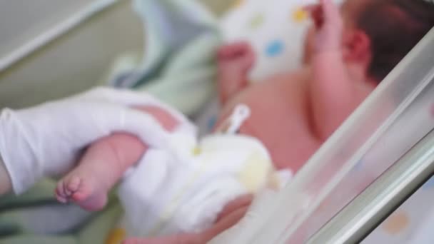 Βρεφική ηλικία, παιδική ηλικία, ιατρική και υγεία, παιδιατρική έννοια - γκρο πλαν των γυναικείων χεριών σε λευκά γάντια καουτσούκ εξέταση νεογέννητο μωρό με κλιπ αφαλό στα πρώτα λεπτά της ζωής στο ιατρικό κρεβάτι — Αρχείο Βίντεο