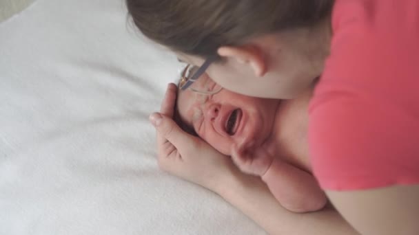 Infanty, kindertijd, moederschap, familie, hygiëne, geneeskunde en gezondheid concept - close-up moeder handen ontkleedt bodysuit pasgeboren wakker baby top uitzicht op witte achtergrond in de eerste minuten van het leven. Stap 3 — Stockvideo