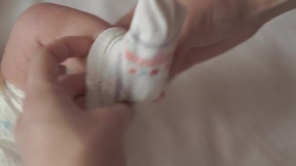 Säuglingsalter, Kindheit, Mutterschaft, Hygiene, Medizin und Gesundheitskonzept - weibliche Handmama zieht Socken über neugeborenes nacktes Baby, das in Windeln auf dem Rücken liegt, mit Bauchnabel eingeklemmt durch medizinischen Clip auf weißem Hintergrund — Stockvideo