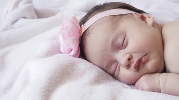 Infancy, childhood, development, medicine and health concept - close-up face of a newborn naked sleeping baby girl lying on her stomach with a bandage and a flower on her head on a pink background. — Stock Video