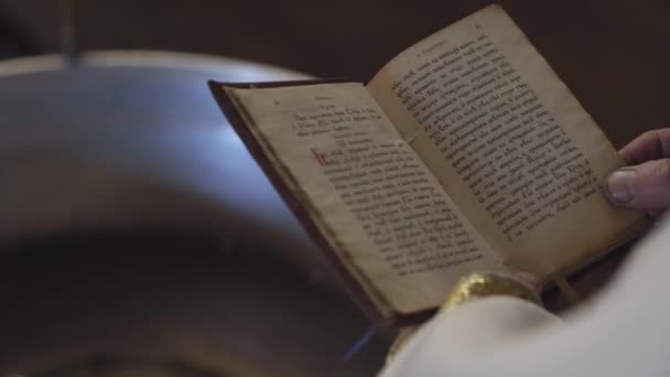 Religion, Christianity, Orthodoxy, ritual, cult, concept - close-up hands of priest in white robes holds treasury book with text in ancient Church Slavonic language performing sacrament of Baptism. — Stock Video