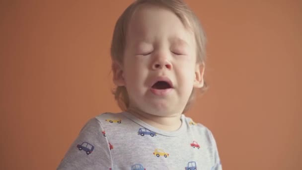 Enfants, célébration, anniversaire, concept de jeux - gros plan petit garçon aux cheveux blonds en costume gris éternue en souriant en dansant en regardant la caméra et en montrant différentes émotions sur fond solide orange. — Video