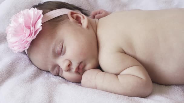 Csecsemőkor, gyermekkor, fejlődés, orvostudomány és egészség koncepció - közelkép egy újszülött meztelen alvó kislányról, aki a hasán fekszik kötszerrel és virággal a fején rózsaszín alapon. — Stock videók