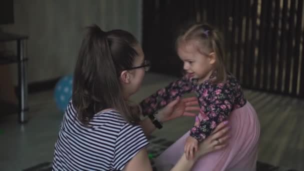 Maternité, enfance, alimentation, nourriture, famille, concept de soins - maman aux cheveux bruns du plan moyen nourrit son enfant de deux ans du Moyen-Orient à partir d'une assiette de cuillère en jean déchiré assis sur le sol — Video