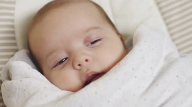 bebek, çocukluk, gelişim, tıp ve sağlık konsepti - Beyaz bir battaniyenin altında sallanan sandalyede uzanan uyanık yeni doğmuş bir bebeğin yakın plan portresi.