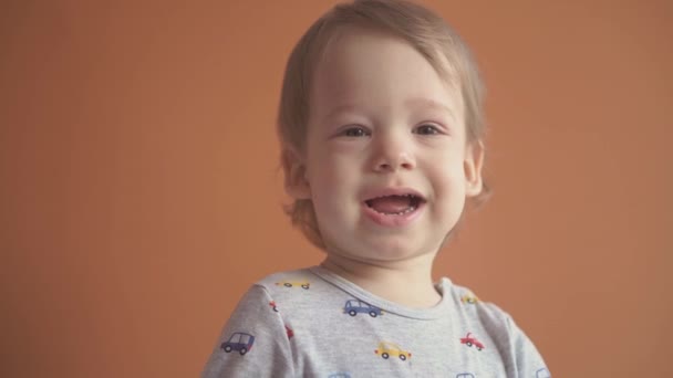 Děti, oslavy, narozeniny, herní koncept - zblízka malý 2-letý blonďatý chlapec v šedém obleku s úsměvem tančící na kameru a ukazující různé emoce na oranžovém pevném pozadí. — Stock video