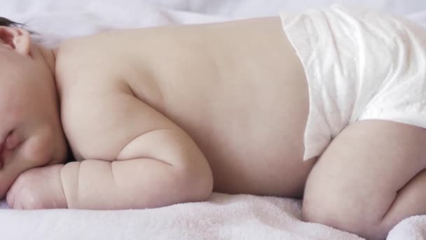 Kindertijd, kindertijd, ontwikkeling, geneeskunde en gezondheid concept - close-up gezicht van een pasgeboren naakt slapende baby meisje liggend op haar buik met een verband en een bloem op haar hoofd op een roze achtergrond. — Stockvideo