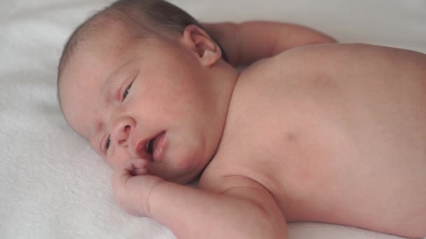 Βρεφική ηλικία, την παιδική ηλικία, την ανάπτυξη, την ιατρική και την υγεία έννοια - close-up πρόσωπο του νεογέννητου γυμνό ηρεμία ξύπνιοι grimaces μωρό βρίσκεται στην πλάτη με τον αφαλό κρατώντας ιατρικό κλιπ σε λευκό μπεζ φόντο — Αρχείο Βίντεο
