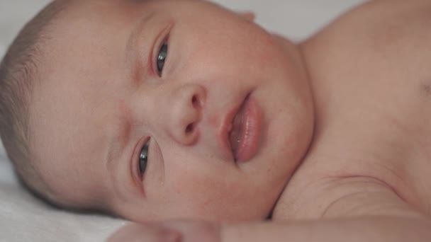 Kindertijd, kindertijd, ontwikkeling, geneeskunde en gezondheid concept - close-up side view gezicht van pasgeboren naakt wakker baby grimaces liggend op de rug met navel houden medische clip op witte achtergrond — Stockvideo